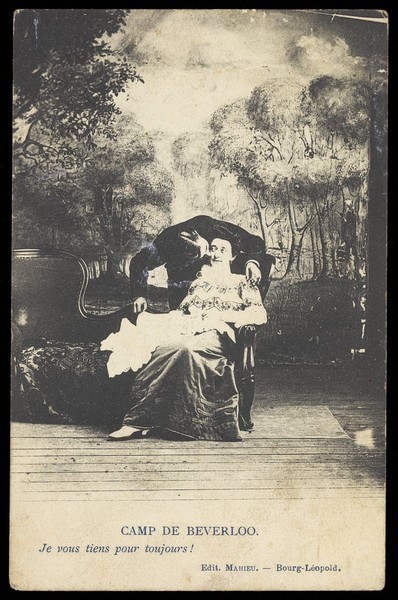 Download the full-sized image of Two amateur actors, one in drag, share a kiss on stage, in front of a detailed backdrop of trees at Beverloo Camp in Belgium. Process print, 190-.