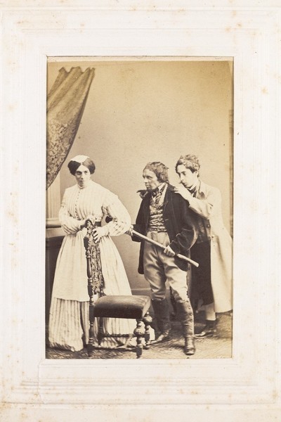 Download the full-sized image of Three men, one in drag, acting out a scene. Photograph, 189-.