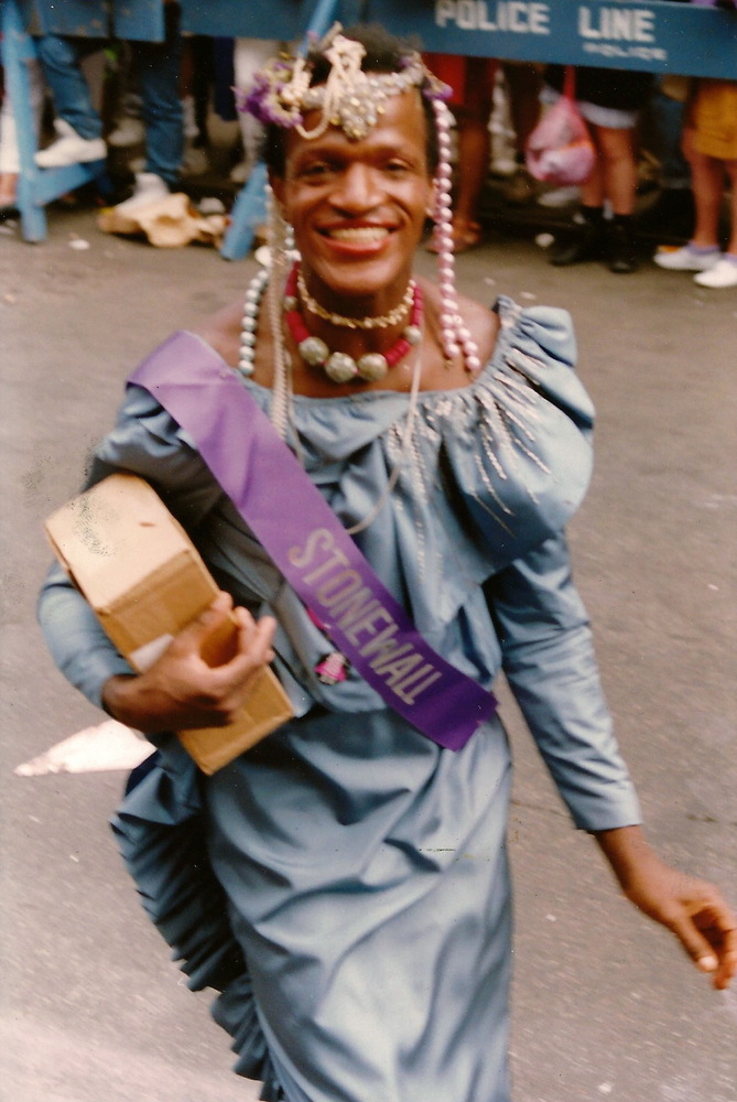 Download the full-sized image of A Photograph of Marsha P. Johnson Wearing a Pearl Headpiece, Blue Dress, and a Purple “Stonewall” Sash
