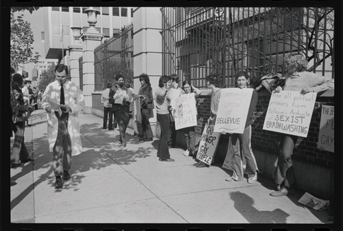 Download the full-sized image of Photograph of Sylvia Rivera and Others Protesting while People in Lab Coats Walk Past