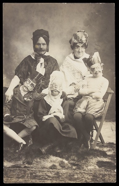 Download the full-sized image of A family, all members wearing grotesque masks, the father in drag. Photographic postcard, ca. 1910.