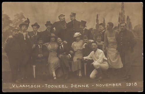 Download the full-sized image of Belgian prisoners of war, some in drag, pose on stage for a group portrait; at Sennelager prisoner of war camp in Germany. Photographic postcard, 1918.