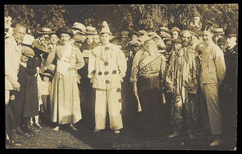 Download the full-sized image of People at Rickmansworth, Herts., some in drag, gather outside at a swimmming gala. Photographic postcard, 1908.