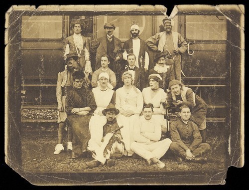 Download the full-sized image of Actors sitting in front of an ambulance train, some in drag. Photograph, 191-.