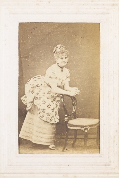 Download the full-sized image of A man in drag resting against a chair. Photograph, 187-.