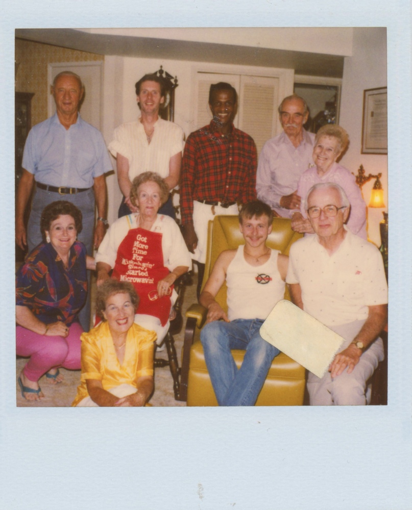 Download the full-sized image of A Photograph of Marsha P. Johnson Posing with a Group in a Living Room, Wearing a Red Flannel and White Pants