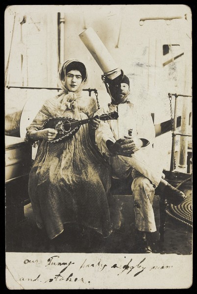 Download the full-sized image of Two sailors (?) on board ship: one in drag is playing a guitar. Photographic postcard, 1907.