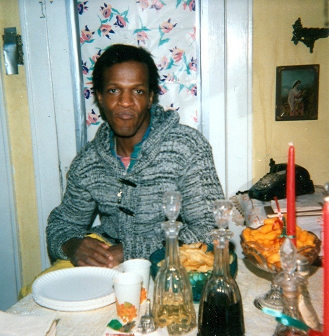 Download the full-sized image of A Photograph of Marsha P. Johnson Sitting at the Kitchen Table Wearing a Gray Sweater