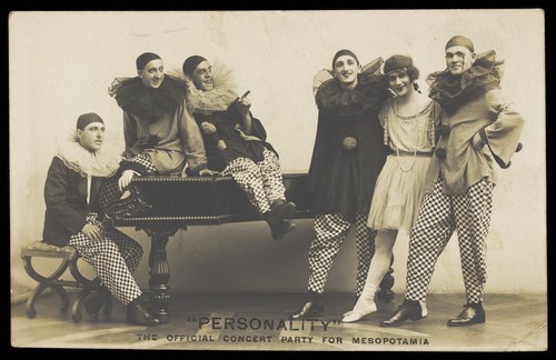 Download the full-sized image of Soldiers, one in drag, performing in the concert party for Mesopotamia, posing around a piano. Photographic postcard by Hana Studios, 191-.