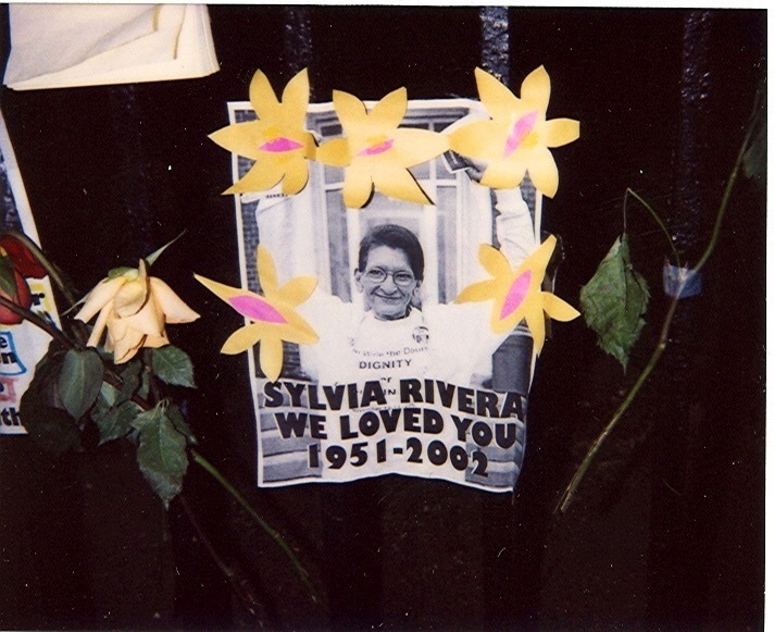 Download the full-sized image of A Photograph of a Poster and Flowers for Sylvia Rivera at Her Memorial Site