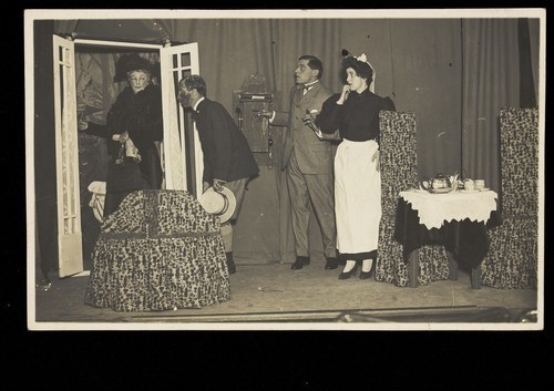 Download the full-sized image of Amateur actors, one in drag, perform a scene on stage. Photographic postcard, 191-.